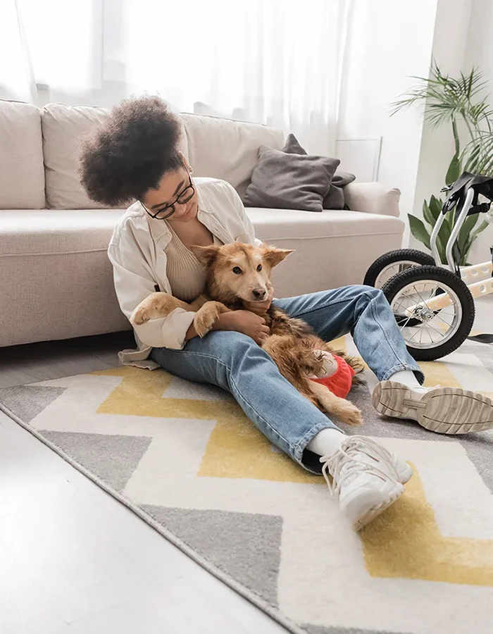disabled-dog-cuddling-with-owner A woman sits on the floor of her living room holding her disabled dog