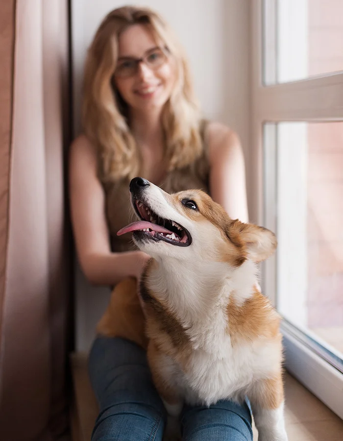 A woman and her corgi sit happily by a window
