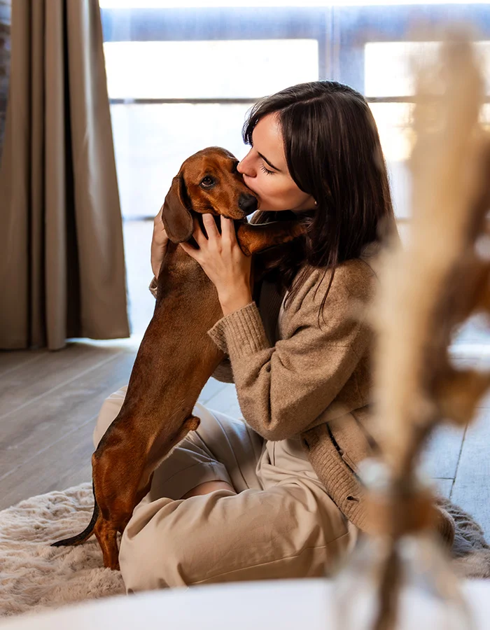 A woman gives her brown dog a kiss while they sit on the floor