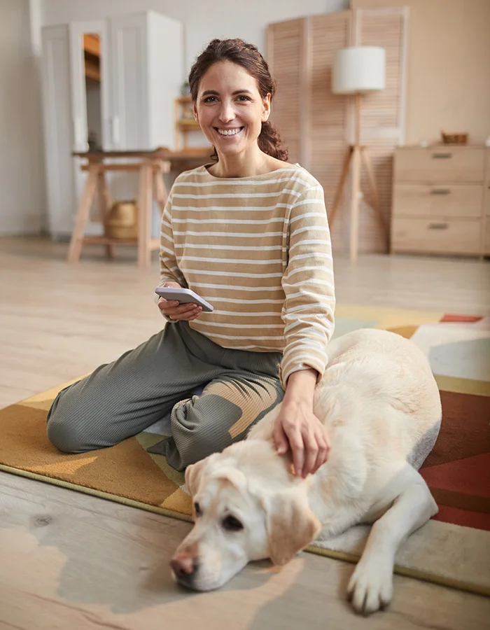 woman-on-phone-petting-dog A happy woman holds her phone and pets her dog while sitting on the floor