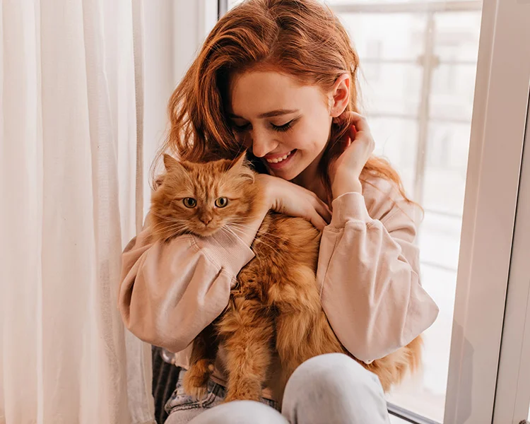A happy young woman cuddles with her orange cat at home