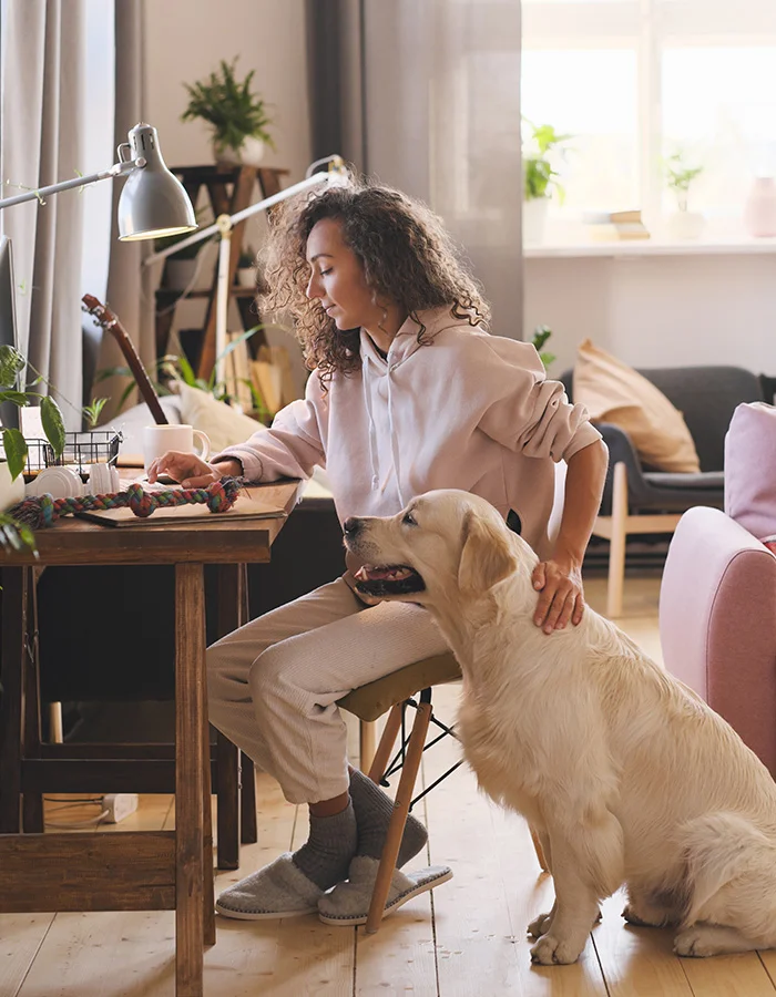 young-woman-home-desk-petting-dog A woman sits at her home desk with her dog beside her