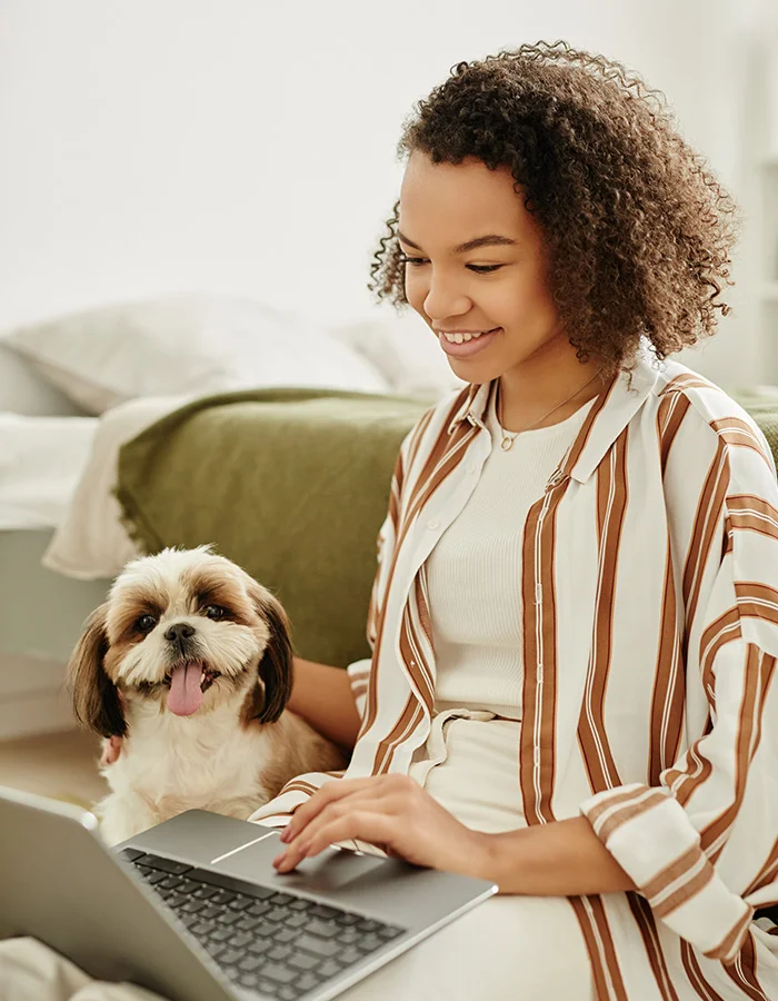 young-woman-on-computer-with-dog A young woman and her dog at home. The young woman is using a laptop.