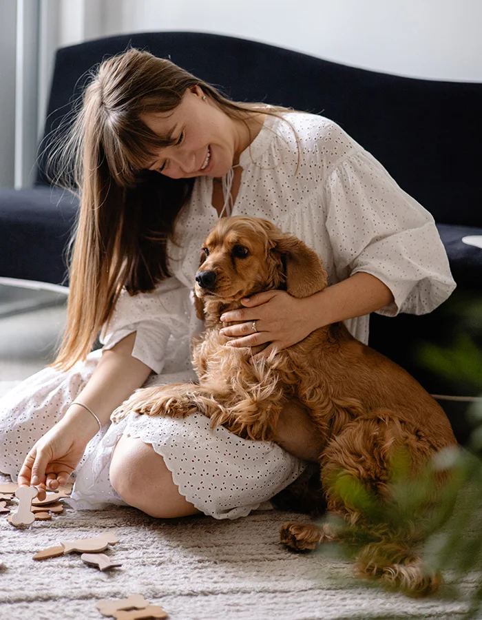 woman-with-spaniel-at-home A happy woman sits on the floor playing with her spaniel dog